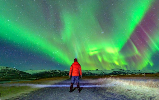 Tourist in red jacket watching northern lights in Norway.