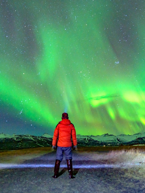 Tourist in red jacket watching northern lights in Norway.