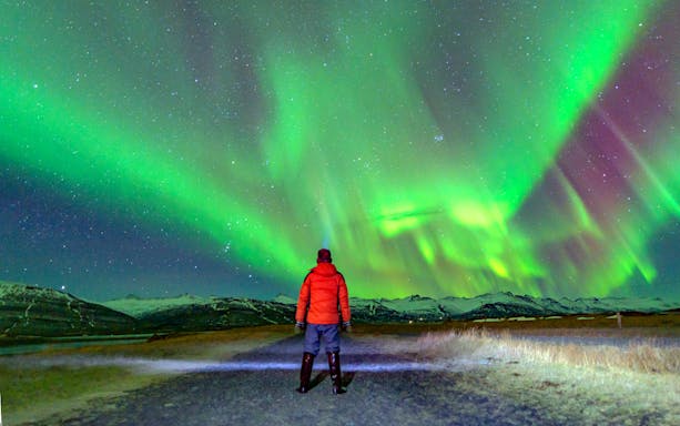Tourist in red jacket watching northern lights in Norway.