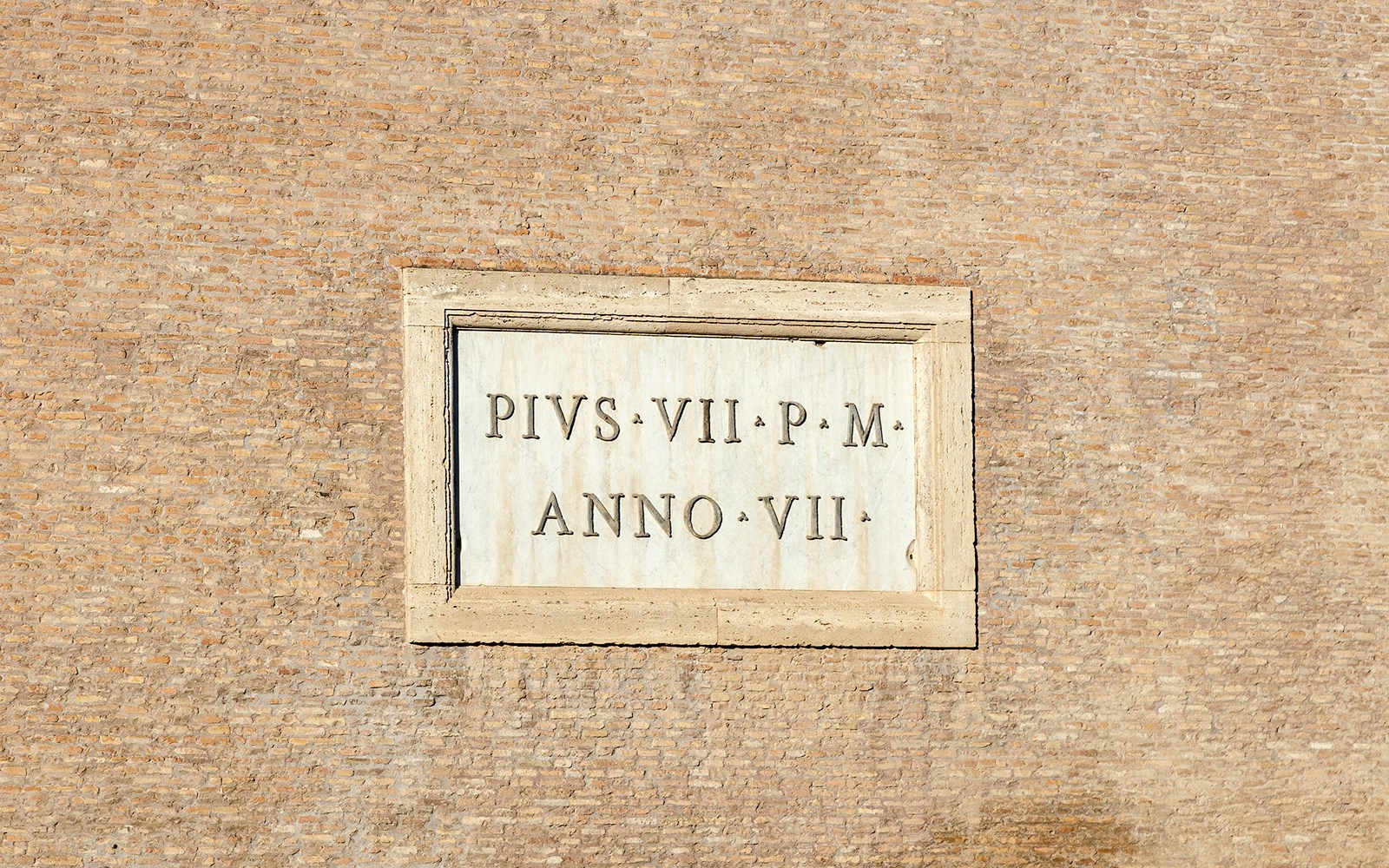 Marble plaque with inscription of Pope Pius VII on a brick wall.