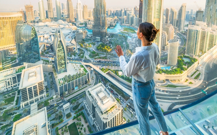 Person enjoying view from Sky Views Edge Walk, overlooking Dubai skyline and Burj Khalifa.