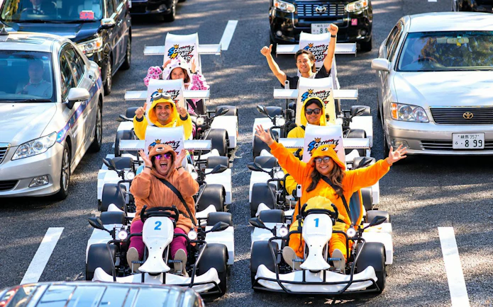 Tourists in costumes driving go-karts on a busy Tokyo street during Shibuya go-kart experience.