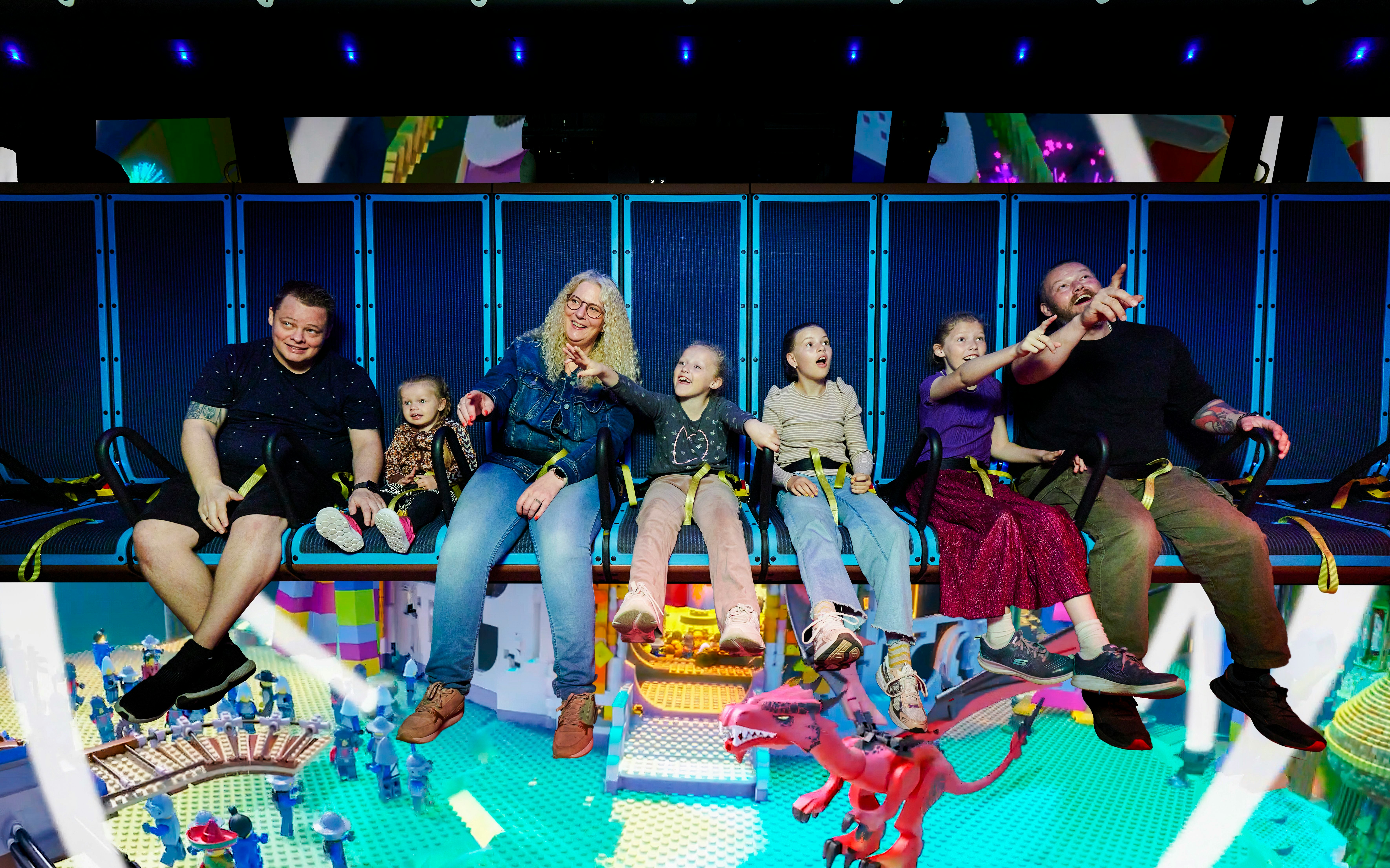 Family enjoying a ride at LEGOLAND Billund with LEGO-themed scenery below.