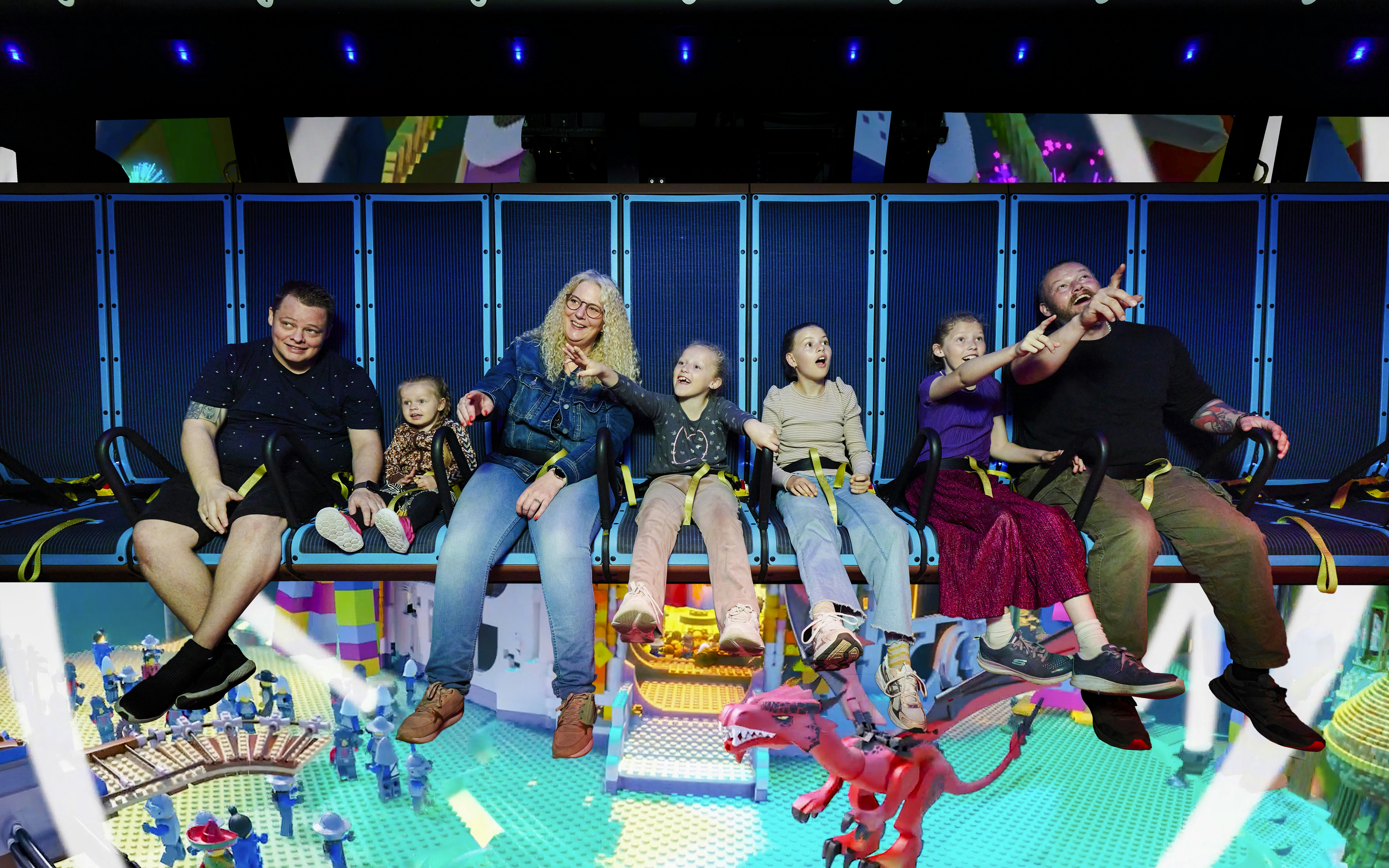 Family enjoying a ride at LEGOLAND Billund with LEGO-themed scenery below.