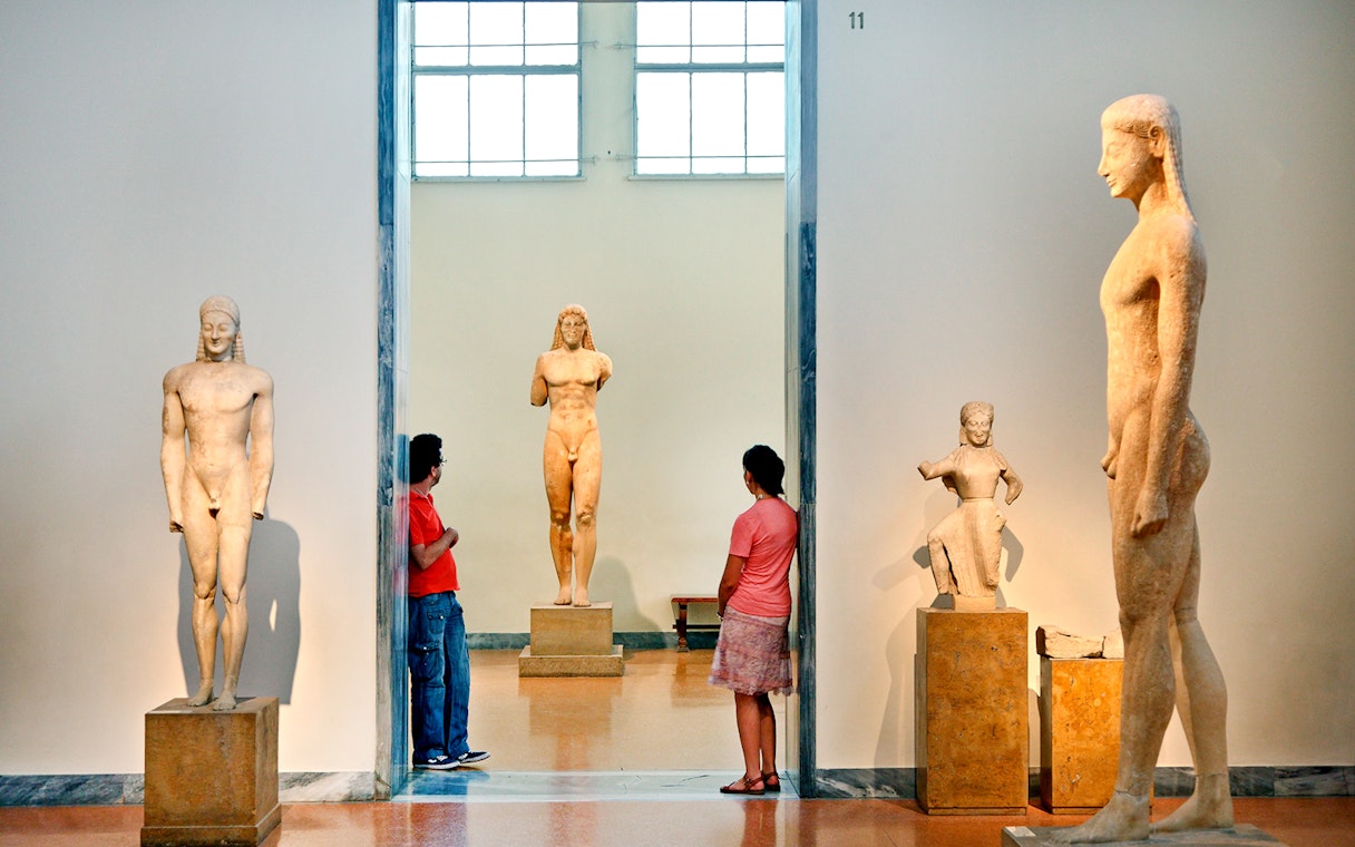 Visitors viewing ancient Greek statues at Athens National Archaeological Museum.