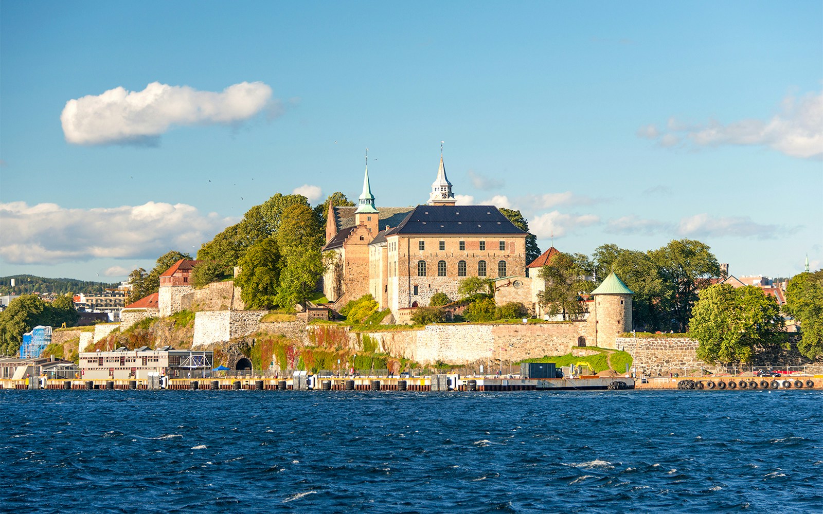 Akershus Fortress in Oslo viewed from the water, surrounded by trees and historic buildings.
