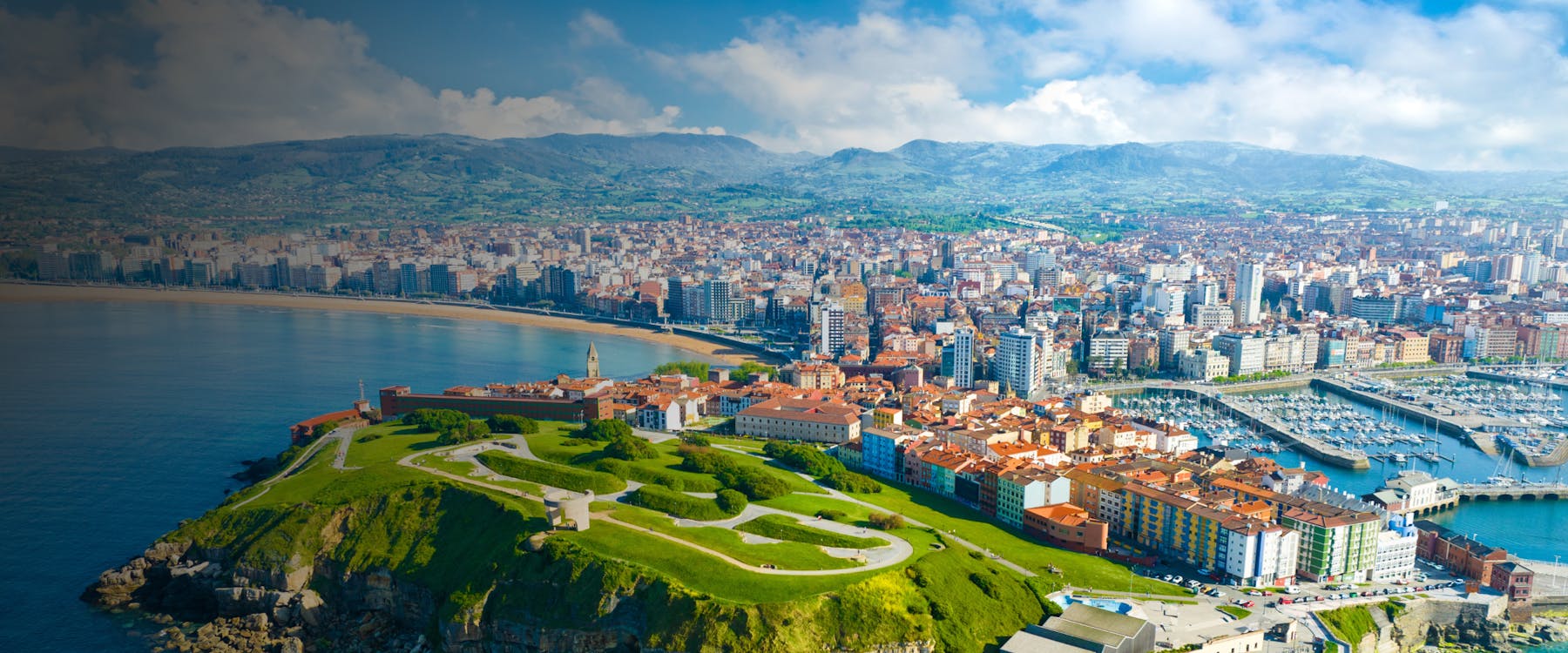 Aerial view of Gijon, Spain, featuring San Lorenzo beach, marina, and historic buildings.