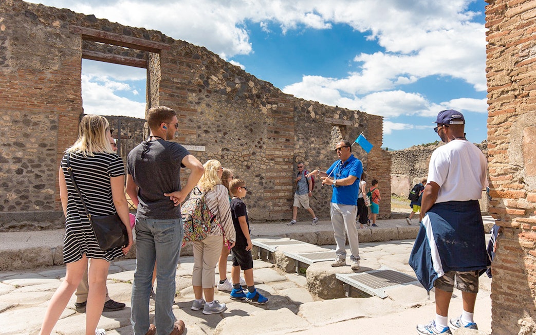 Visitors listening to a tour guide in Pompeii ruins, Italy.