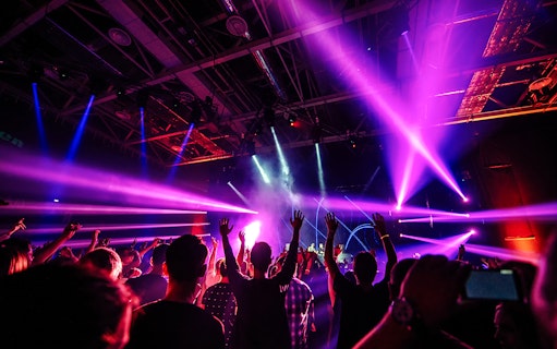 Nightclub scene with people dancing under vibrant purple and blue lights.
