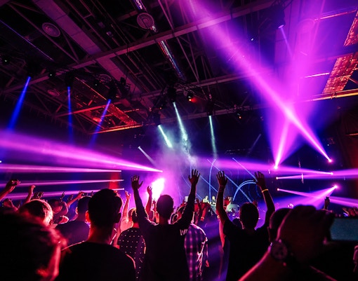 Nightclub scene with people dancing under vibrant purple and blue lights.