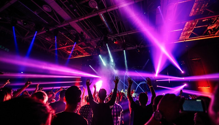 Nightclub scene with people dancing under vibrant purple and blue lights.