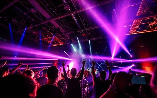 Nightclub scene with people dancing under vibrant purple and blue lights.