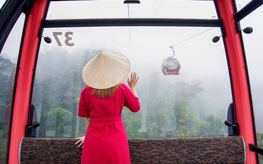 Woman in red dress and conical hat on cable car to Ba Na Hills, Da Nang, Vietnam.