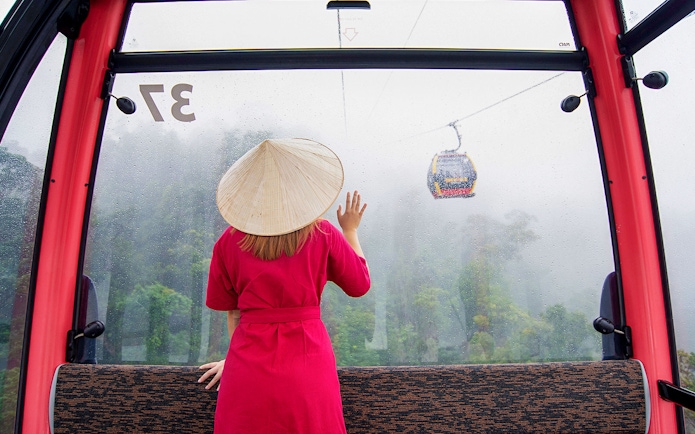 Woman in red dress and conical hat on cable car to Ba Na Hills, Da Nang, Vietnam.