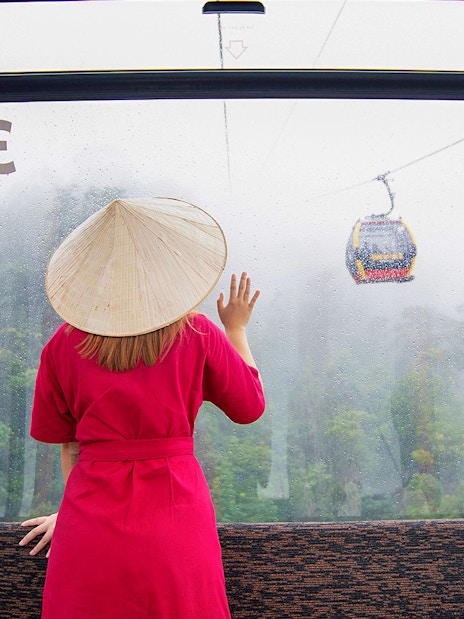 Woman in red dress and conical hat on cable car to Ba Na Hills, Da Nang, Vietnam.