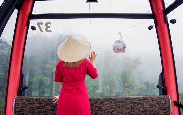 Woman in red dress and conical hat on cable car to Ba Na Hills, Da Nang, Vietnam.