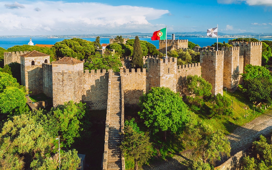 São Jorge Castle in Lisbon with stone walls, towers, and Portuguese flag.