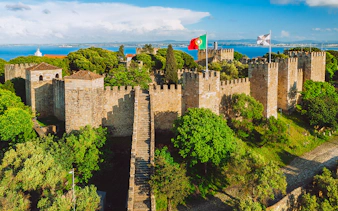 São Jorge Castle in Lisbon with stone walls, towers, and Portuguese flag.