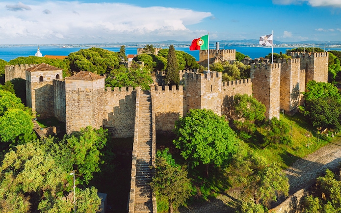 São Jorge Castle in Lisbon with stone walls, towers, and Portuguese flag.