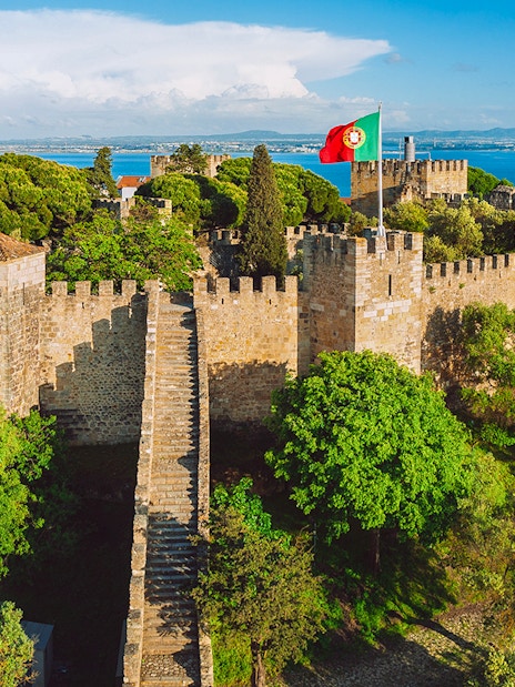 São Jorge Castle in Lisbon with stone walls, towers, and Portuguese flag.