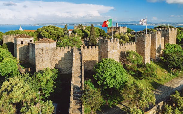 São Jorge Castle in Lisbon with stone walls, towers, and Portuguese flag.