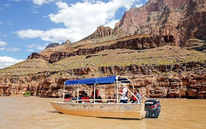 Boat ride on the Colorado River with tourists, Grand Canyon West Rim cliffs in background.