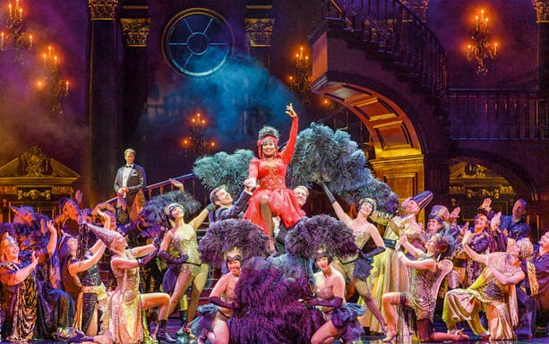 Performers in vibrant costumes on stage during "Rebecca - The Musical" production.