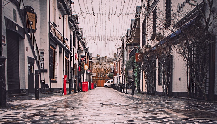 Cobbled street of Ashton Lane in Glasgow with hanging lights and shop signs.