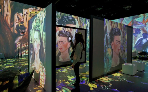 Frida Kahlo's artwork projected in immersive exhibition with visitor taking photo.
