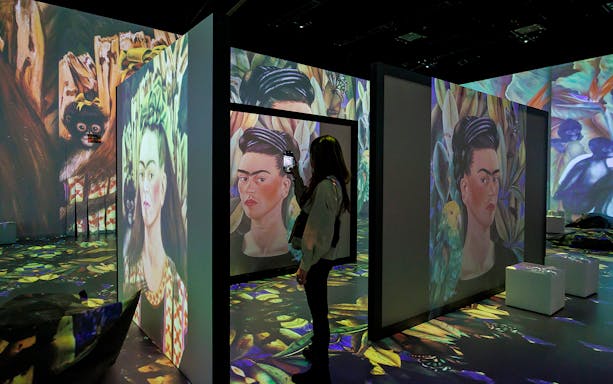 Frida Kahlo's artwork projected in immersive exhibition with visitor taking photo.