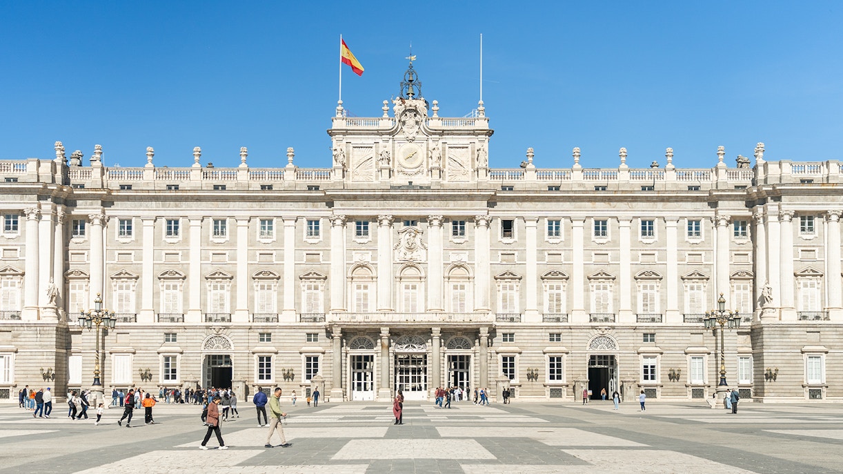 Royal Palace of Madrid exterior with ornate architecture and tourists exploring the grounds.