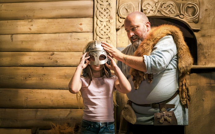Costumed guide helps child try on Viking helmet at The Viking Museum, Stockholm.