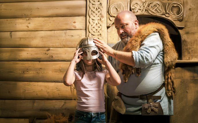 Costumed guide helps child try on Viking helmet at The Viking Museum, Stockholm.