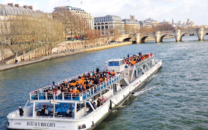 Seine River cruise boat with passengers near Parisian architecture and bridge.