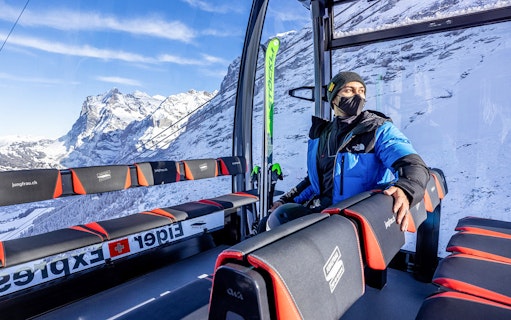 Person inside Eiger Express cable car with snowy Jungfrau mountains in the background.