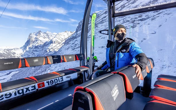 Person inside Eiger Express cable car with snowy Jungfrau mountains in the background.