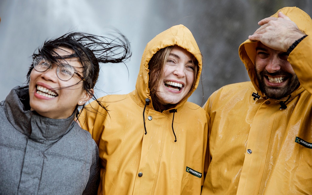 Tourists in raincoats smiling near a waterfall on Milford Sound day trip from Queenstown.