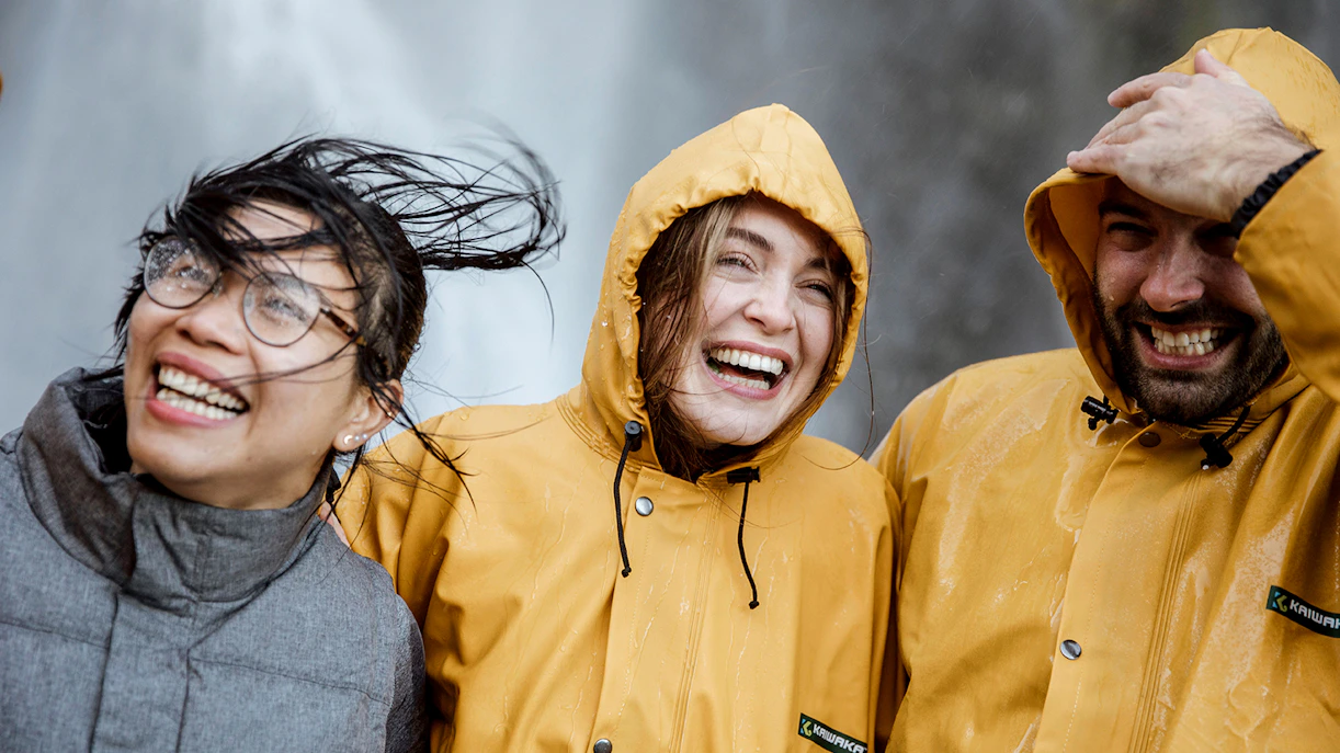 Tourists in raincoats smiling near a waterfall on Milford Sound day trip from Queenstown.