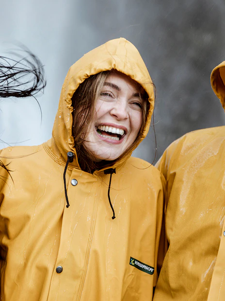 Tourists in raincoats smiling near a waterfall on Milford Sound day trip from Queenstown.