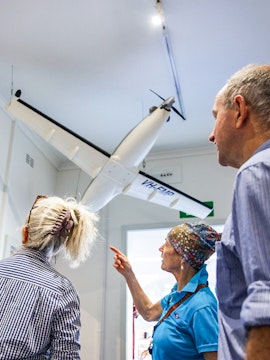 Tour guide explaining model aircraft display at aviation museum.
