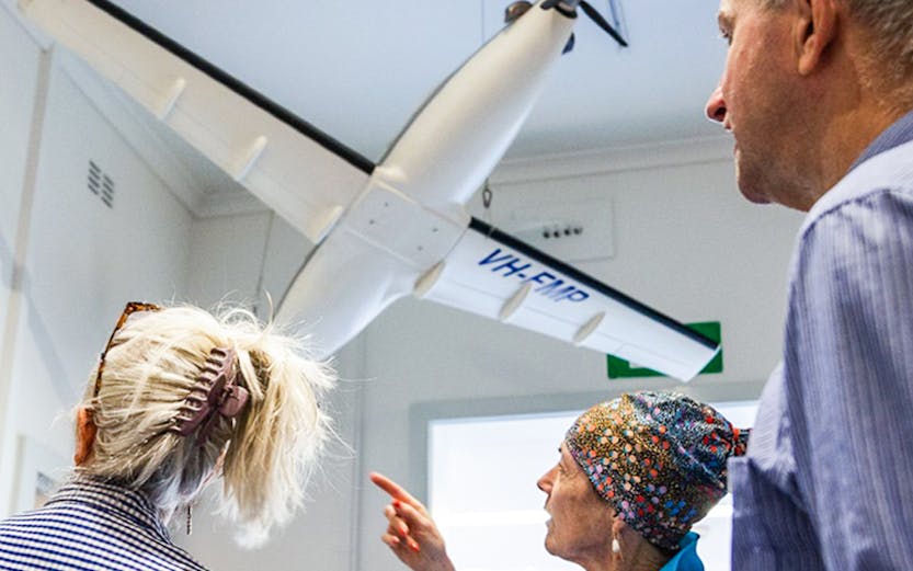 Tour guide explaining model aircraft display at aviation museum.