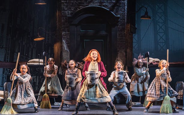 Children performing a musical number from "Annie" on stage with brooms and buckets.