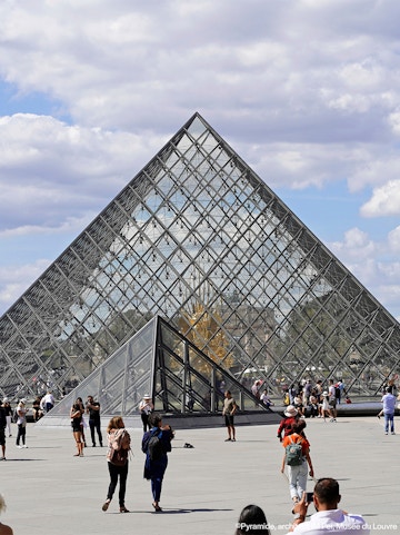 Louvre Museum glass pyramid entrance with visitors in Paris.