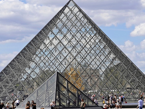 Louvre Museum glass pyramid entrance with visitors in Paris.
