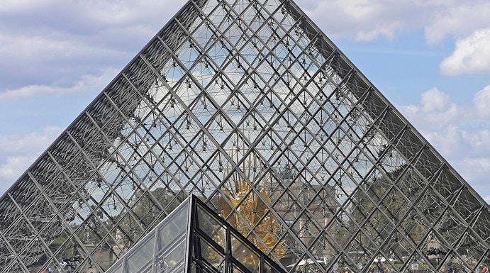 Louvre Museum glass pyramid entrance with visitors in Paris.