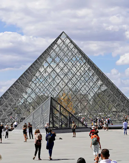 Louvre Museum glass pyramid entrance with visitors in Paris.
