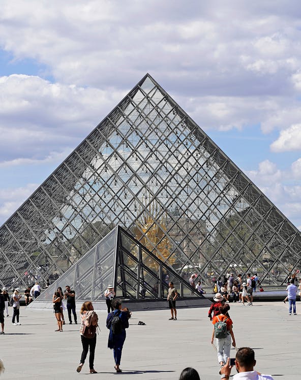 Louvre Museum glass pyramid entrance with visitors in Paris.