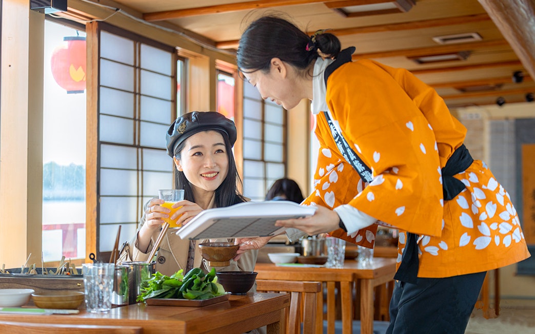 Server in traditional attire serves a guest on a Yakatabune dinner cruise in Japan.