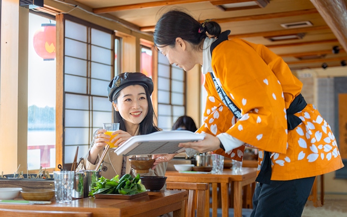Server in traditional attire serves a guest on a Yakatabune dinner cruise in Japan.