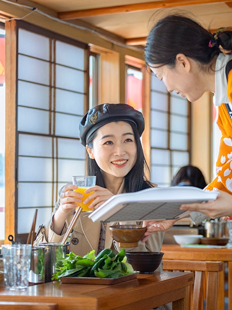 Server in traditional attire serves a guest on a Yakatabune dinner cruise in Japan.